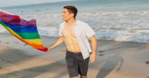 man flying rainbow flag on beach