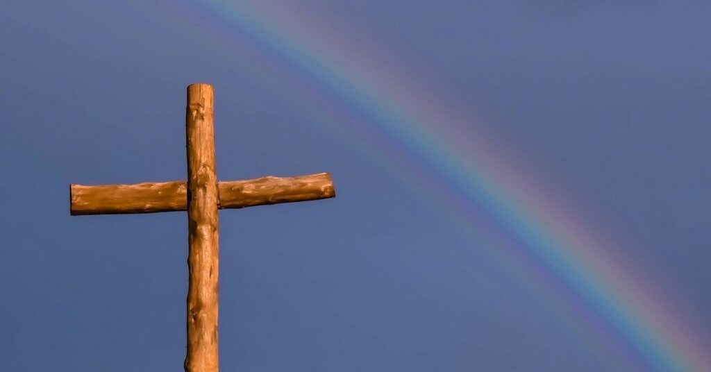 wooden cross in front of a rainbow